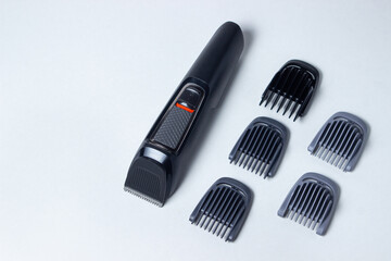Fototapeta na wymiar Beard trimmer on a white background. Different sized attachments are placed next to the trimmer. Beard care. Male style