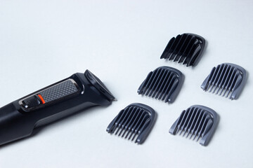 Fototapeta premium Beard trimmer on a white background. Different sized attachments are placed next to the trimmer. Beard care. Male style
