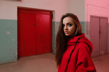 A beautiful girl of 20-25 years old in a red sweatshirt posing in an underground room. 