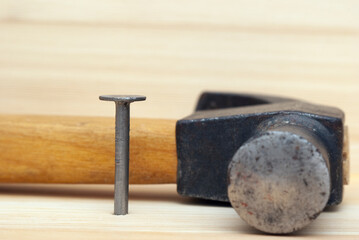 One iron nail and hammer on wooden background