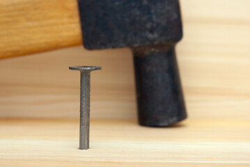 One iron nail and hammer on wooden background