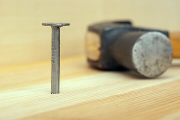 One iron nail and hammer on wooden background