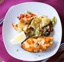 delicious salmon steak with potato garnish with slice of lemon on white plate in restaurant
