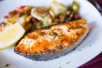 delicious salmon steak with potato garnish with slice of lemon on white plate in restaurant