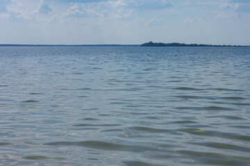 Lake on a sunny day with blue sky and white clouds. Waves and glare on the surface of the water.
