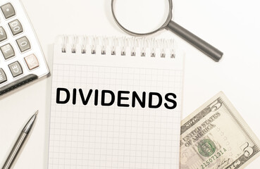 text DIVIDENDS written on notepad with calculator, pensil, magnifier and dollars. Business concept.