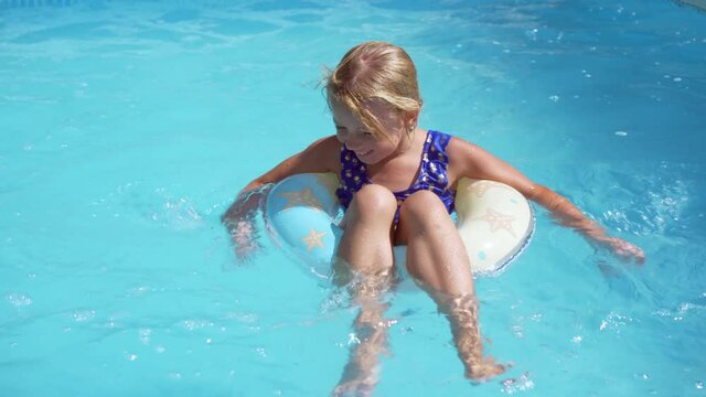 Little girl is resting in the hotel pool. Floats on a rubber ring and smiles. Swimming on a hot day.