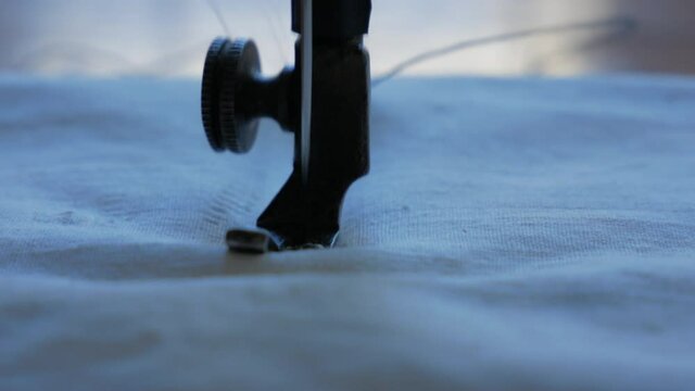 Sewing Machine Needle in Motion. Close-up of sewing machine needle rapidly moves up and down. The tailor sews white fabric on the sewing workshop. The process of sewing fabric.