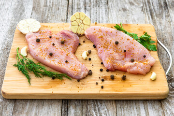 Raw Turkey steak is on a chopping Board with seasoning.
