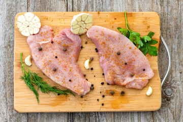 Raw Turkey steak is on a chopping Board with seasoning.