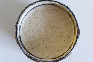Selbstgemachter Sauerteig Starter mit Luftblasen in rundem Glas von oben gesehen, weißer...