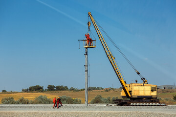 a railroad crane with a cradle lifted workers on the installation of electrical networks on a pole during the construction of a new railroad track, on sunny day and blue sky.