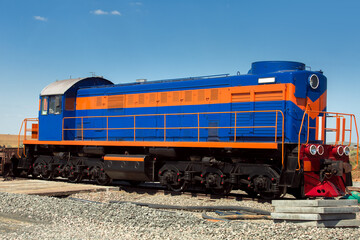 Fototapeta na wymiar a blue shunting diesel locomotive with an orange stripe, a deck type locomotive stands on a railroad bed strewn with rubble, nobody.