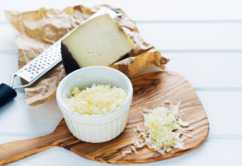 Bowl with shredded cheese on a chopping board. Piece of cheese and grater. Copy space.