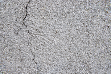 Pale plaster painted wall with grit and cracks. Cracked wall closeup photo. Architecture detail background. Empty concrete wall. Grungy surface of painted cement. Abstract grainy texture