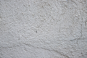White plaster painted wall with grit and grain. Cracked wall closeup photo. Architecture detail background. Empty concrete wall. Grungy surface of painted cement. Abstract grainy texture
