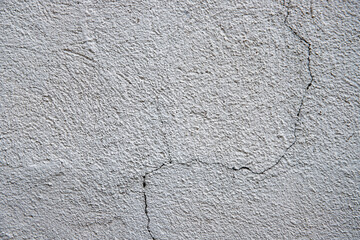 White plaster painted wall with curvy crack. Cracked wall closeup photo. Architecture detail background. Empty concrete wall. Grungy surface of painted cement. Abstract grainy texture