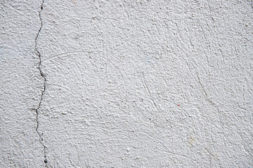 White plaster painted wall with grain and cracks. Cracked wall closeup photo. Architecture detail background. Empty concrete wall. Grungy surface of painted cement. Abstract grainy texture