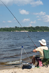 A man is fishing on a spinning rod on the river bank on a sunny summer day.