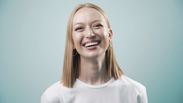 Happy female with natural white teeth laughing to camera, selective focus. Smiling woman face with perfect smile in light blue background. Smile healthy teeth concept, 4k