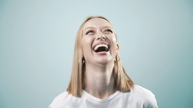 Happy female with natural white teeth laughing to camera, selective focus. Smiling woman face with perfect smile in light blue background. Smile healthy teeth concept, 4k