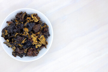 Dried black mushroom in bowl on wooden table. Wood ear mushroom pile top view photo. Dry mushroom for soup or garnish ingredient. Natural healthy food from chinese market. Asian cuisine dish