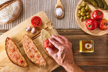 Top view of a set of ingredients and the preparation of a typical bread with olive oil Pa amb Oli from Mallorca,  action of rub the ramillet tomato on the bread with the hand.