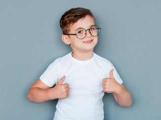 A child with glasses gives a thumbs-up. A kid likes the glasses. Little boy approves. Copy space.