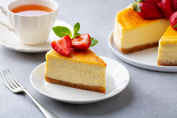 Cheesecake dessert with fresh strawberries and cup of tea. Grey background. Close up.