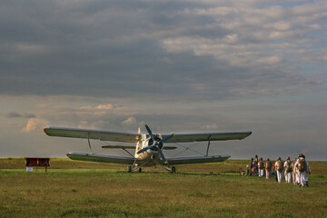 parachutists landing on the plane with a propeller on the field against the background of clouds