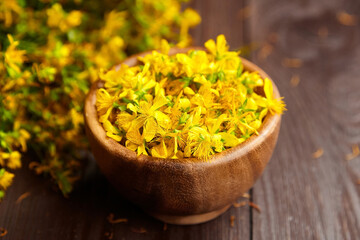 St. John’s wort (Hypericum perforatum) petals in wooden bowl on brown table. Medicinal plant with...