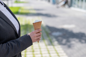 Faceless business woman walks outdoors and eats vanilla ice cream on a sunny summer day. Close-up of female hands with ice cream cone.