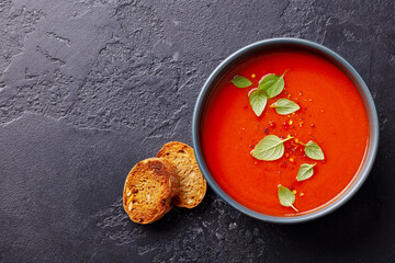 Tomato soup with basil in a bowl. Dark background. Copy space. Top view.