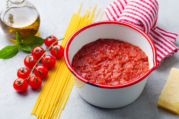 Traditional tomato sauce in saucepan with spaghetti pasta. Grey background. Close up.