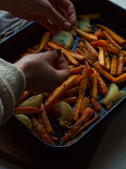 Rustic roasted carrots and onion on black oven tray in natural light on farm table.