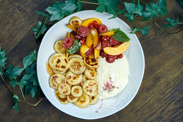 Mini pancakes with yogurt and fruit in a white plate on a wooden background. Delicious food for breakfast