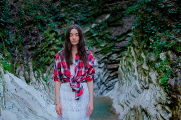 Young woman in white dress and plaid shirt practicing breathing yoga pranayama outdoors in moss gorge. Unity with nature concept.