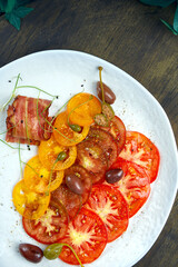 Tomato carpaccio with capers and bacon in a white plate on a wooden background. Italian appetizer