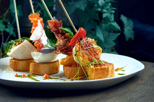 Classic Spanish antipasto - pintxos or tapas with shrimp, camembert, salmon and jamon in a white plate. Selective focus