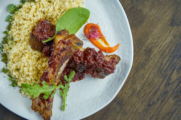 Appetizing grilled pork ribs with bulgur in a white plate on a wooden background. Selective focus. Roasted ribs