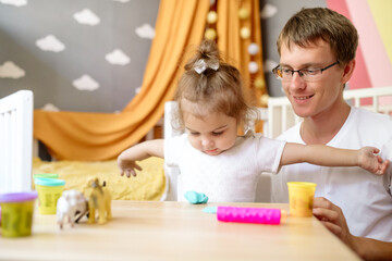 Obraz na płótnie Canvas Little funny girl 2 years old plays plasticine and toys with her father in the children's room