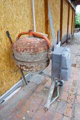 Old orange rusty cement mixer and yellow sawdust wall. Detail on construction site.