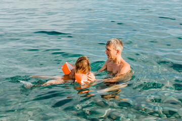 Grandfather teaching toddler girl swimming in sea