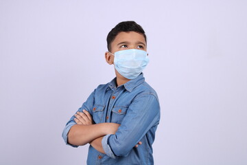 Cute little Indian boy with folded hands wearing surgical mask, looking up, isolated over white background