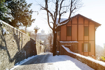 A snow covered lane with a building and walls on either side,, and glimpses of a distant town