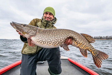 Success pike fishing. Happy fisherman with big fish trophy at boat