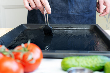 Men's hands hold a brush and grease a baking sheet with oil, in the home kitchen, there are...