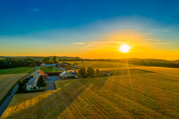 Glowing sunset aerial view at a farm house with a huge field in foreground.