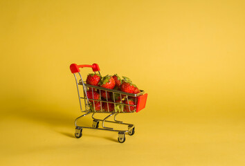 metal cart with strawberries on a yellow isolated background with space for text