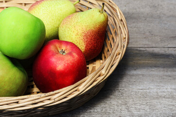 Ripe fruit in a wicker basket on a rough wooden surface. Apples and pears in a rustic style.